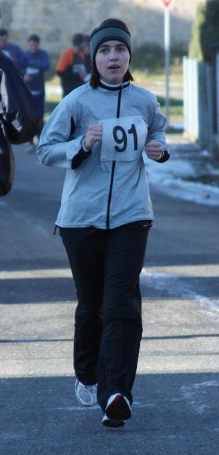 bežící žena v šedivé bundě s číslem 91 na prsou